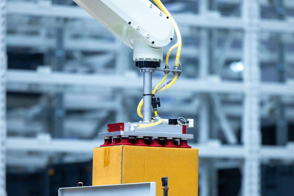 An industrial robotic arm using a vacuum gripper to lift a cardboard box